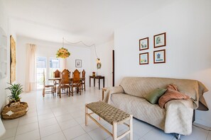 A living room with a sofa, a wooden bench, a dining table with chairs, and a small side table with a plant. - Villa Sousa by Dreamplaces (Albufeira)