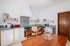 A compact kitchen with a microwave, toaster, and stove. There are wooden chairs and a table with a glass serving tray. - Villa Sousa by Dreamplaces (Albufeira)