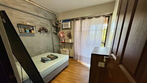 Een compacte slaapkamer met een enkel bed, een klein nachtkastje, een ventilator en een raam met gordijnen.
