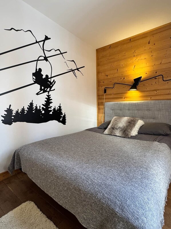 Un dormitorio con cama, cabecera, un adhesivo mural de telesilla y un aplique.