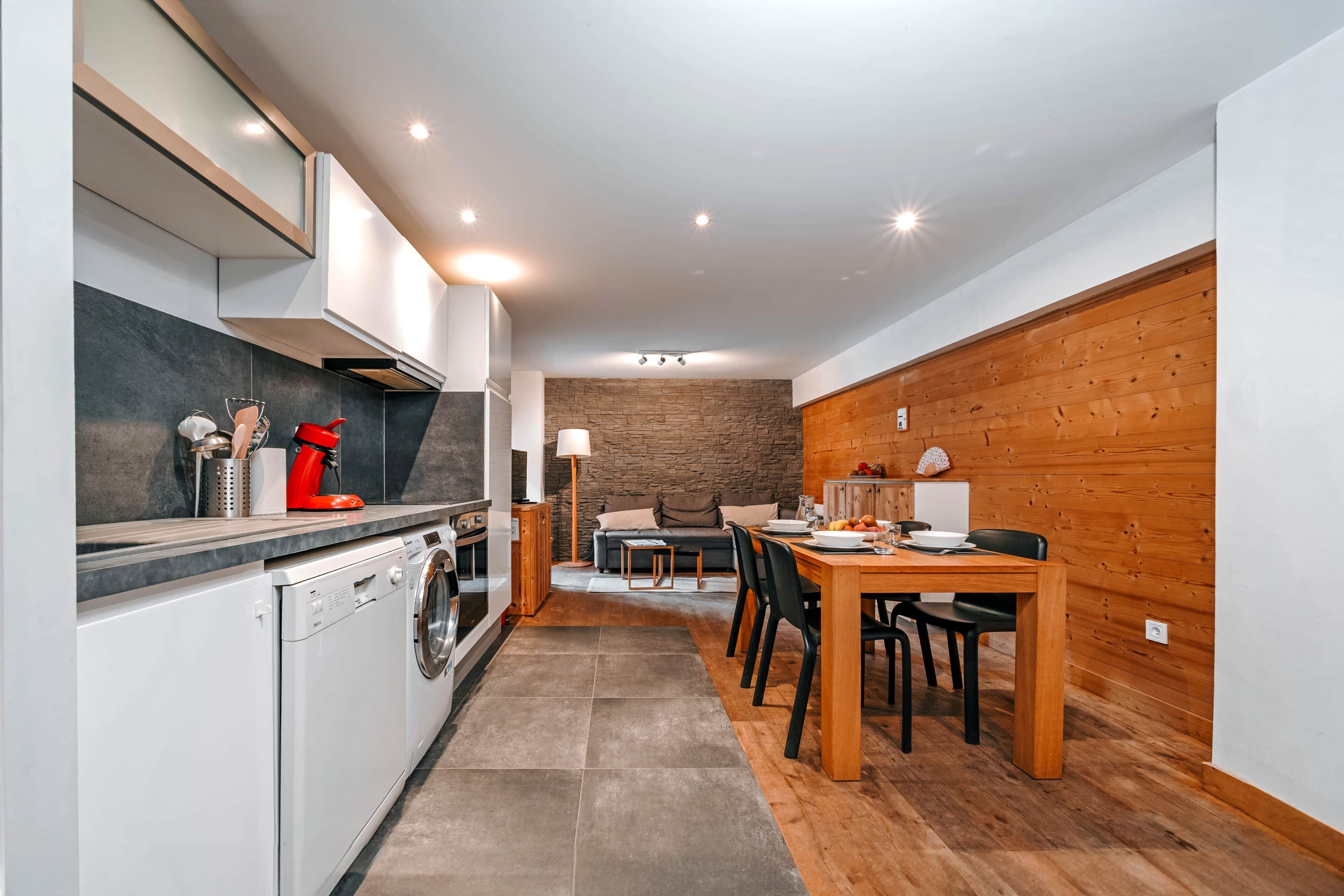 Una cocina moderna con horno integrado, lavavajillas y una tetera roja sobre la encimera.
