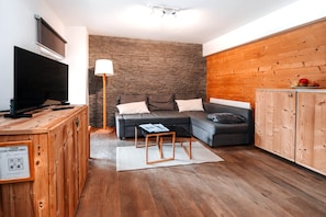 A modern living room with a sectional sofa, a flat-screen TV, a lamp, and a wooden cabinet. - Le Bel Alp - The Perfect Mountain Getaway (Les Deux Alpes)