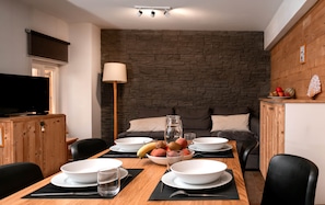 A dining area with a table set for two, a television, and a stone wall in the background. - Le Bel Alp - The Perfect Mountain Getaway (Les Deux Alpes)