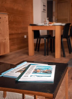 Ein Holztisch mit Broschüren in einem Raum mit Holzwänden und einem Essbereich im Hintergrund.