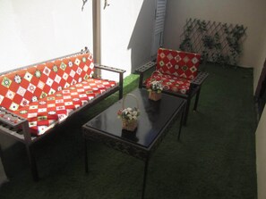 Un patio con un sofá y una silla, ambos con cojines estampados, y una mesita con una cesta y flores.