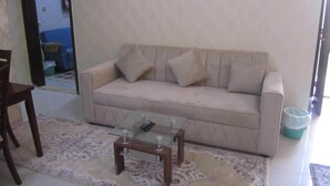 A living room with a beige sofa, a glass coffee table, and a patterned rug. - العين الهيلي مصباح بيت 13 (Al Ain)