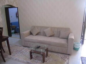 Uma sala de estar com um sofá bege, uma mesa de centro de vidro e um tapete estampado.