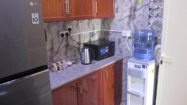 A kitchen with wooden cabinets, a stainless steel refrigerator, a microwave, and a water dispenser. - العين الهيلي مصباح بيت 13 (Al Ain)