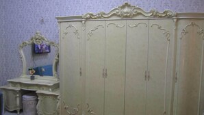 A room with a large armoire, a vanity with a mirror, and a small table with a vase. - العين الهيلي مصباح بيت 13 (Al Ain)