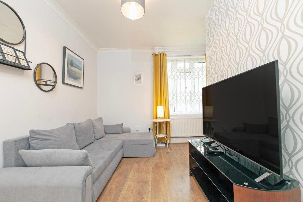 Een woonkamer met een grijze modulaire bank, een flatscreen televisie op een houten dressoir en behang met een patroon.