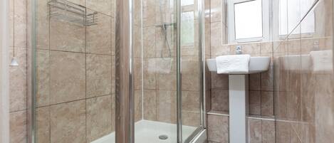 A bathroom with a glass-enclosed shower, a white pedestal sink, and beige tiled walls.