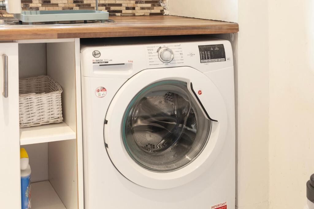 Màquina de rentar amb càrrega frontal, panell de control, cistella i ampolla de detergent.