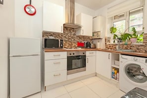 Cozinha com armários brancos, micro-ondas, forno, máquina de lavar e janela com plantas.