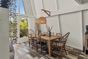 A dining area with a wooden table and chairs, a hanging light fixture, and a view of the outdoors. - Coastal A-Frame Retreat | 2BR/2BA | 5-Min Walk to Beach |  Pet Friendly (Sanibel)