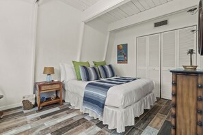 Ein Schlafzimmer mit Bett, Nachttisch, Lampe, Wandbild und Kleiderschrank.