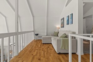 Ein modernes Interieur mit Holzboden, weißen Wänden, einem weißen Sofa mit Kissen und einem kleinen Tisch mit einer Lampe.