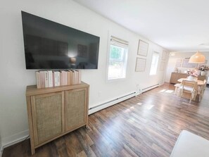A spacious living room with hardwood flooring, a flat-screen TV mounted on a wooden cabinet, and a dining area with a table and chairs. - White Lake Cottage | Whitehall Lakeside Charm (Whitehall)