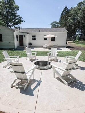 An outdoor patio with Adirondack chairs arranged around a fire pit. - White Lake Cottage | Whitehall Lakeside Charm (Whitehall)
