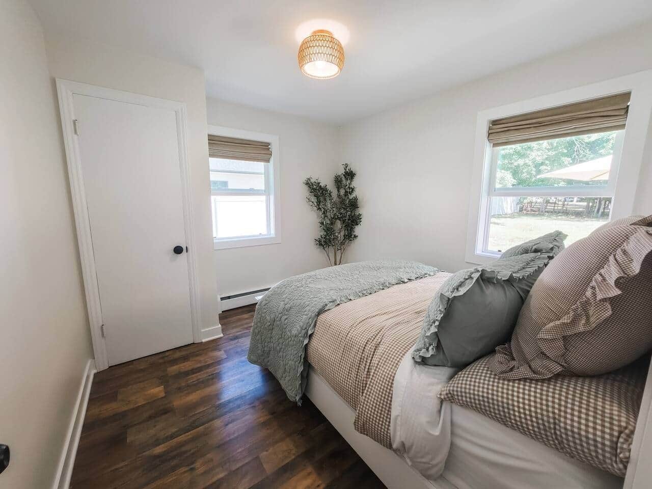 A bedroom with a bed, a door, a window, and a ceiling light fixture.