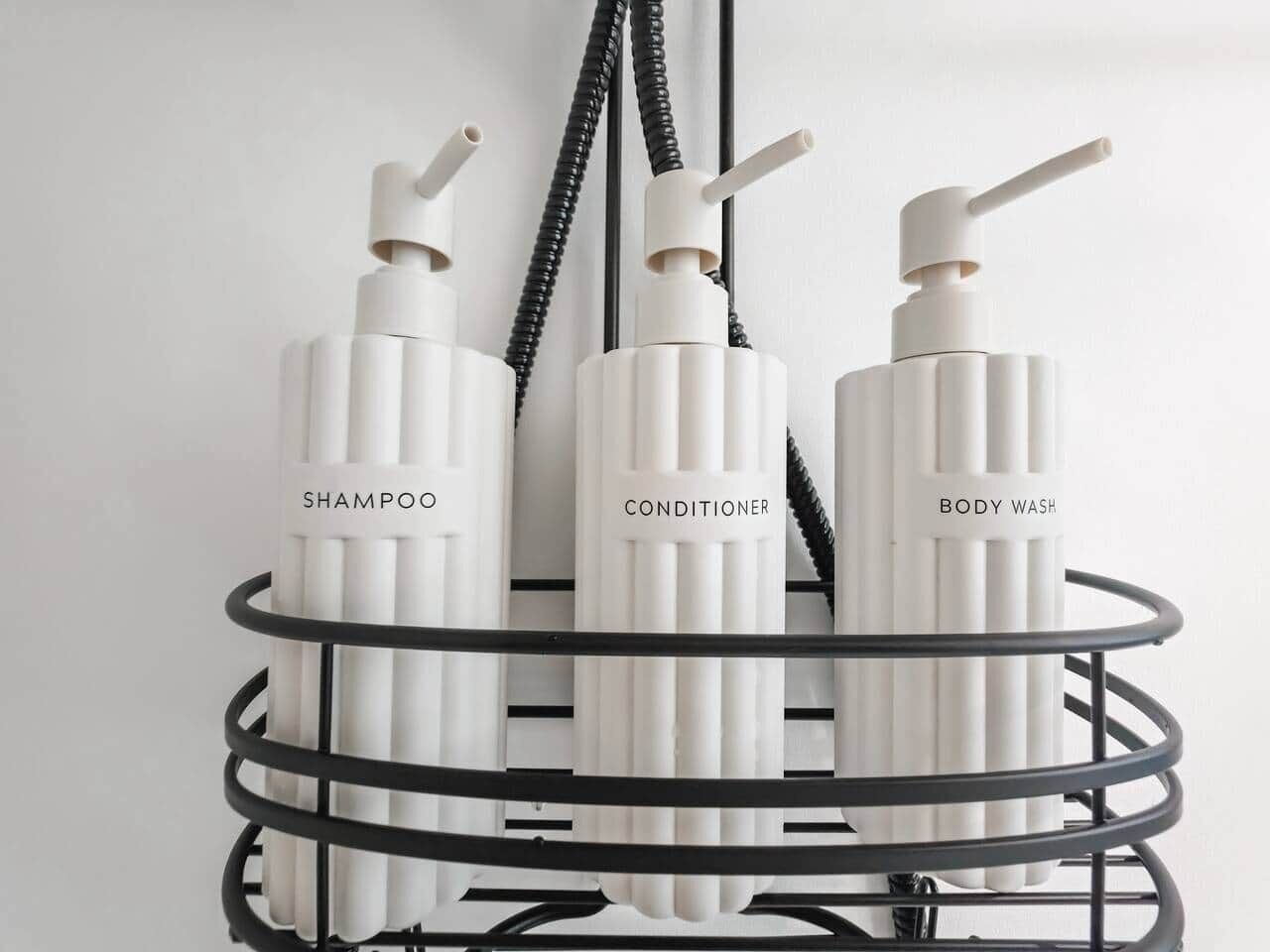 En badeværelseshylde med tre toiletartikler mærket 'SHAMPOO', 'CONDITIONER' og 'BODY WASH'.