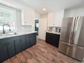 A modern kitchen with dark cabinets, a stainless steel refrigerator, and a wooden floor. - White Lake Cottage | Whitehall Lakeside Charm (Whitehall)