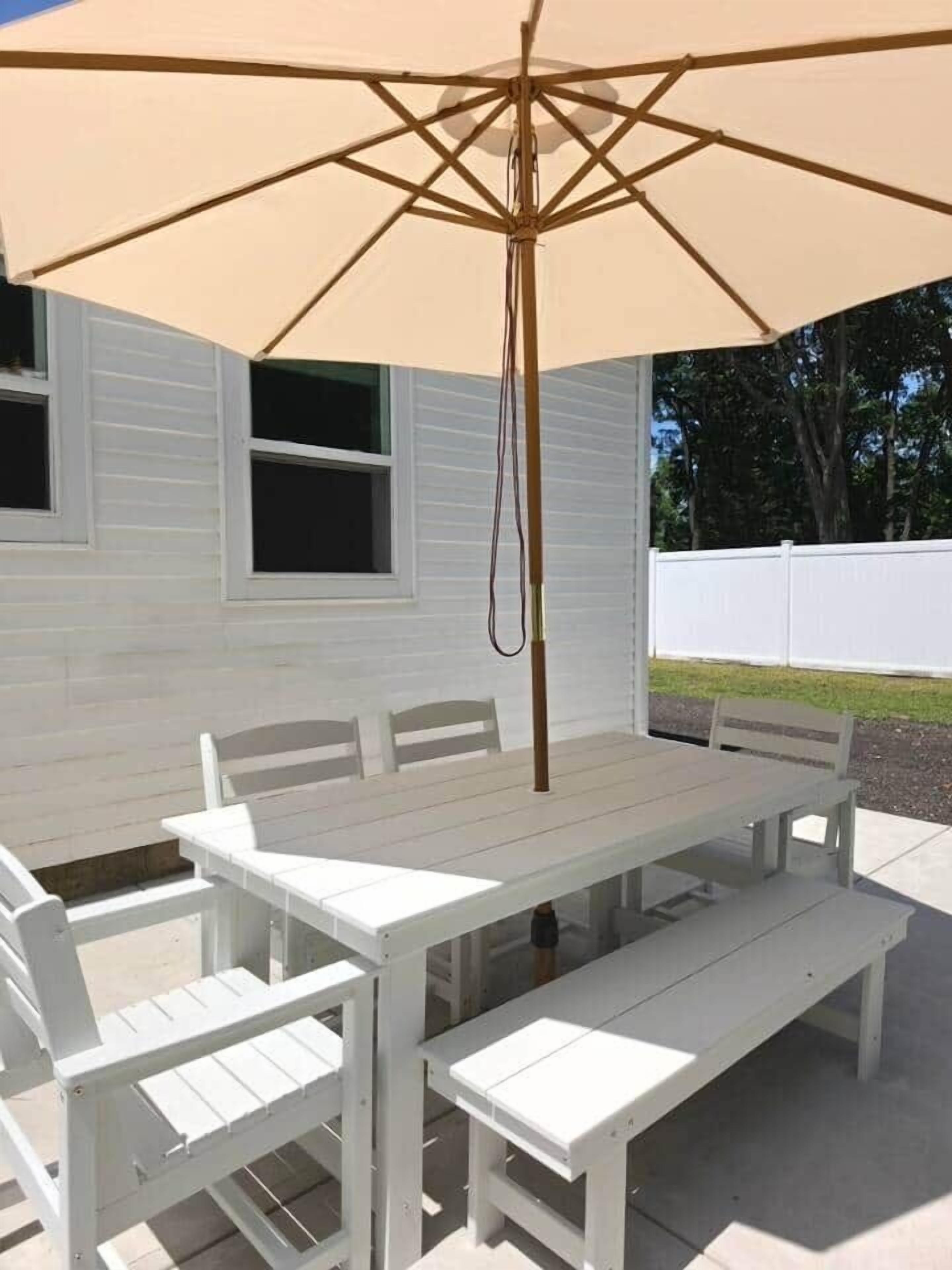 A white wooden patio table with benches, an umbrella, and a hanging light fixture.