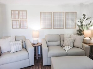 A living room with two sofas, a coffee table, and a side table with lamps. There are four framed pictures on the wall.