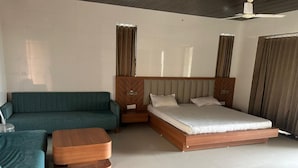 Quarto de hotel moderno com uma cama grande, um sofá, uma mesa de centro de madeira e uma mesa de cabeceira.