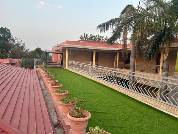 A rooftop terrace with a red roof, a green lawn, and a white railing. - Balaji Upvan Resort (Bavla)
