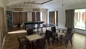 Uma sala com mesa de bilhar, mesa de pingue-pongue e várias cadeiras.