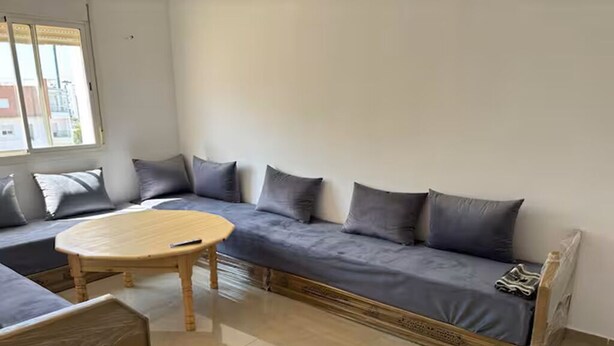 Een kamer met een zithoek, een ronde tafel en een raam met uitzicht op gebouwen.