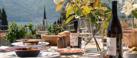 An outdoor dining table set with plates, glasses, and a bottle of wine, overlooking a mountainous landscape.