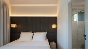 A modern hotel room with a large bed, two bedside lamps, a small bedside table, and a glass door leading to a shower area. - MC residence (Tremezzo)