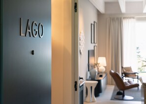 Ein Hotelzimmer mit einer Tür mit der Aufschrift 'LAGO' und einer Sitzecke mit einem Sessel und einem Tisch.
