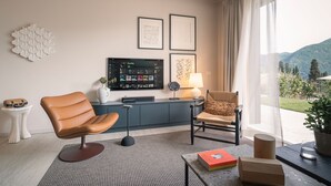 A modern living room with a leather chair, a sofa, a flat-screen TV, and a view of a mountainous landscape through large windows. - MC residence (Tremezzo)