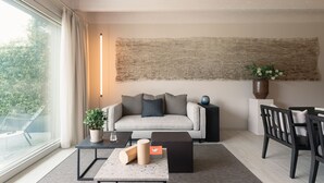 A modern living room with a sofa, a coffee table, a side table, and a chair. There is a large abstract painting on the wall, a potted plant, and a vase with flowers. - MC residence (Tremezzo)