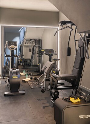 Ein Fitnessstudio mit verschiedenen Trainingsgeräten, darunter eine Hantelbank, ein Kabelzuggerät und ein Laufband.