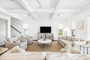 A modern living room with a flat-screen TV, two sofas, a coffee table, and a staircase. - Elegant Pet-Friendly Coastal Retreat with Private Pool, Cabana, & Elevator (Seacrest West)