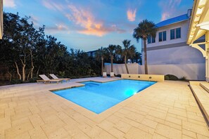 A rectangular swimming pool with a tiled deck, surrounded by palm trees and a wooden fence. - Elegant Pet-Friendly Coastal Retreat with Private Pool, Cabana, & Elevator (Seacrest West)