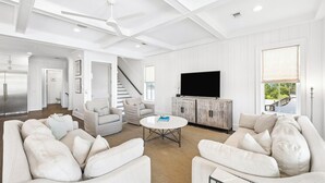 A spacious living room with a large flat-screen TV, a staircase, and a view of the outdoors. - Elegant Pet-Friendly Coastal Retreat with Private Pool, Cabana, & Elevator (Seacrest West)