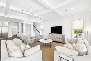 A spacious living room with a large flat-screen TV, a staircase, and a view of the outdoors. - Elegant Pet-Friendly Coastal Retreat with Private Pool, Cabana, & Elevator (Seacrest West)