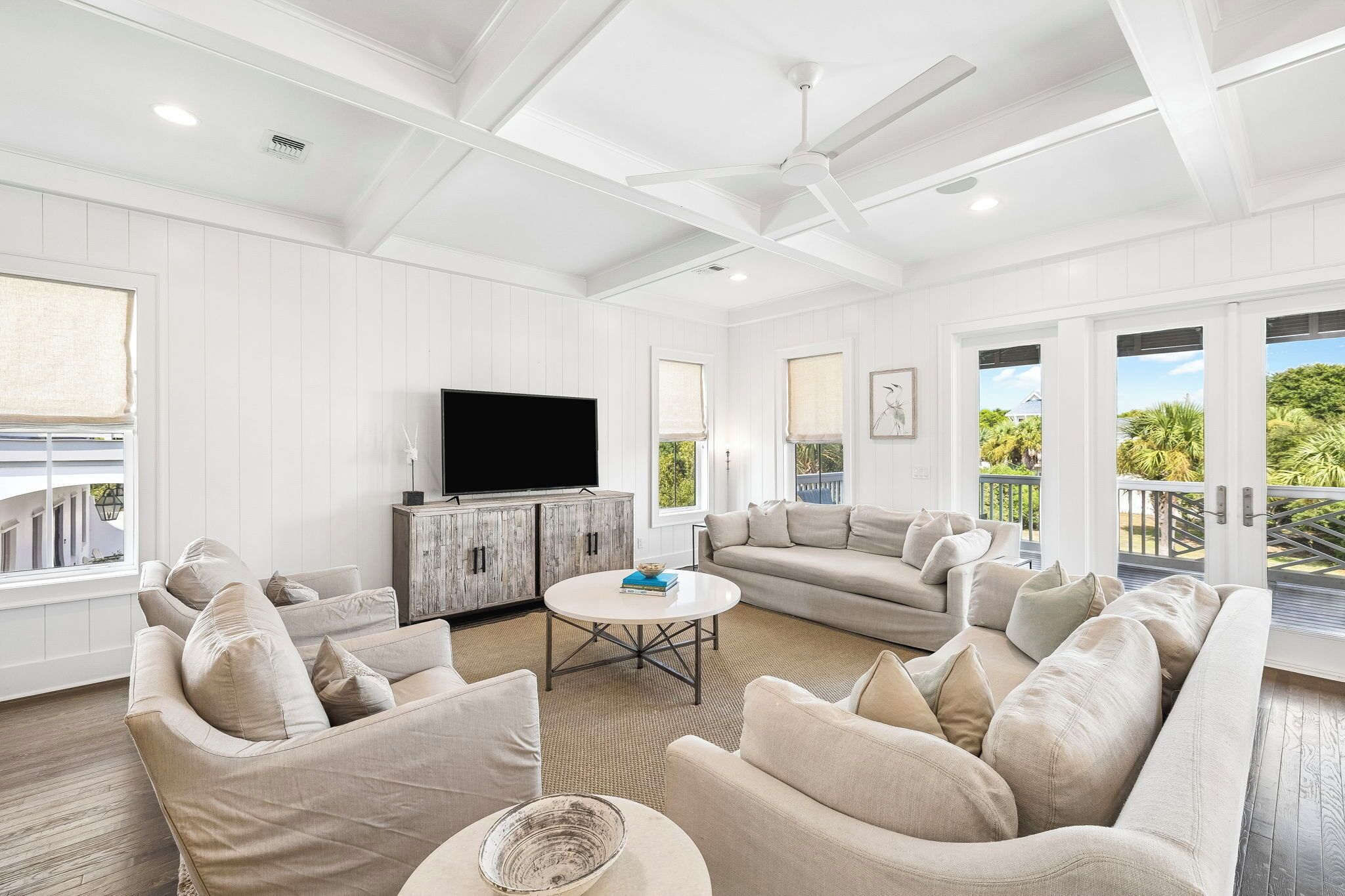 A spacious living room with a large flat-screen TV, a round coffee table, and a sofa set.