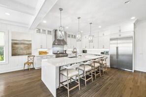 A modern kitchen with white cabinetry, a large island with bar stools, stainless steel appliances, and pendant lighting. - Elegant Pet-Friendly Coastal Retreat with Private Pool, Cabana, & Elevator (Seacrest West)