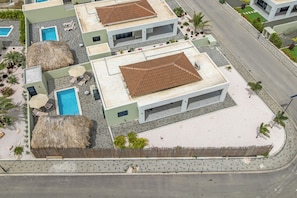 A residential area with multiple houses, a swimming pool, and a paved road. - Villa Santi Mambo Beach With Privatepool (Willemstad)