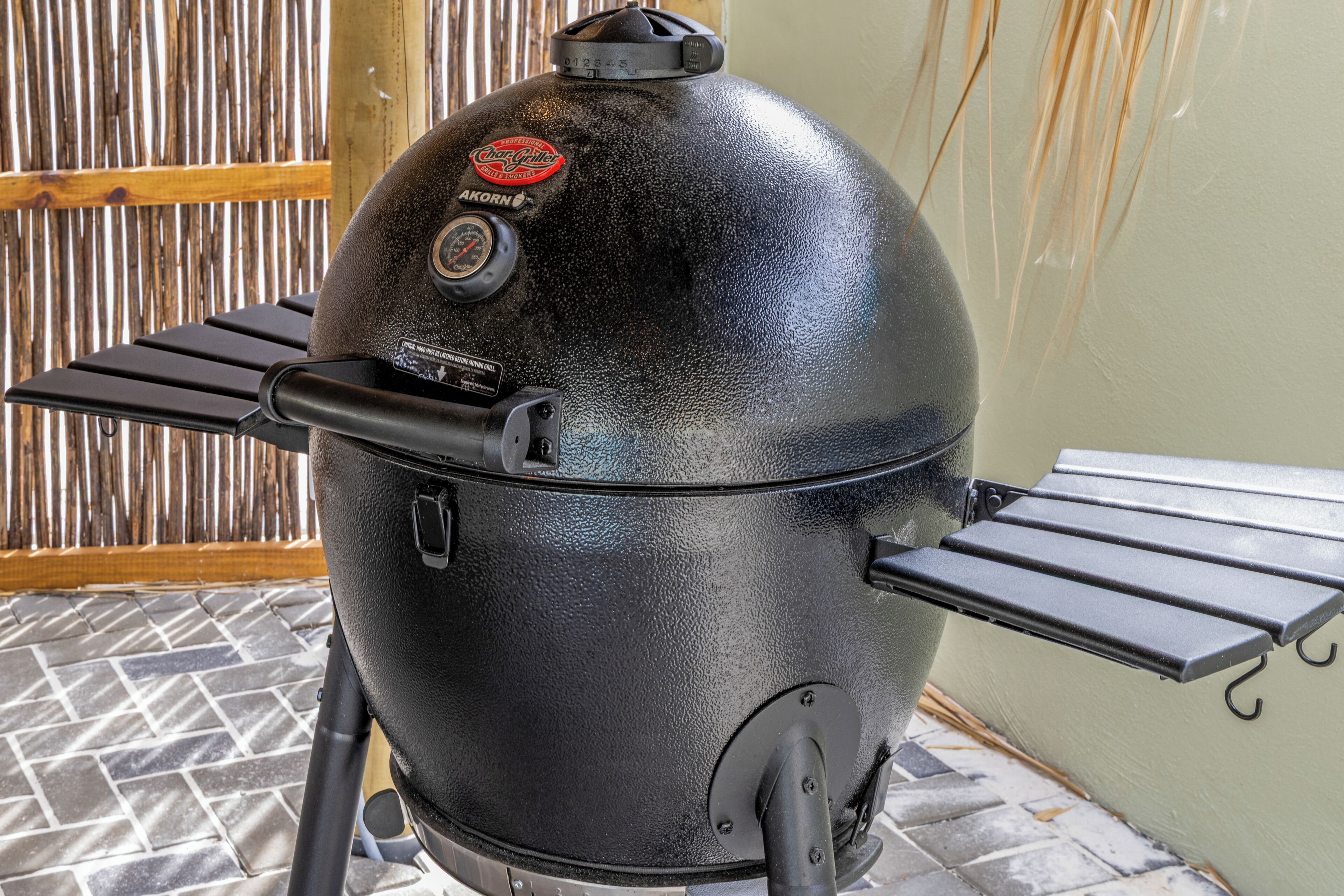 A black Char-Broil gas grill with two side shelves, positioned on a tiled patio.