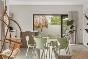 A modern dining area with a large window, a hanging chair, and a dining table with chairs. - Villa Santi Mambo Beach With Privatepool (Willemstad)