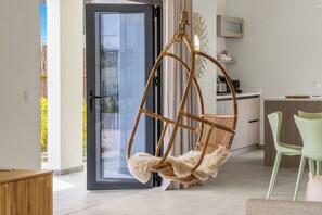 A modern living room with a wicker hanging chair, a green chair, and a kitchen area in the background. - Villa Santi Mambo Beach With Privatepool (Willemstad)