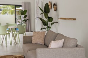 Een woonkamer met een bank, stoelen, een eettafel en grote planten.