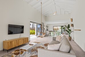 Uma sala de estar ampla com uma televisão grande, um console de madeira, um sofá e uma cadeira suspensa.