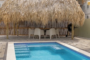 A pool area with a thatched roof structure, a table with chairs, and a grill. - Villa Santi Mambo Beach With Privatepool (Willemstad)
